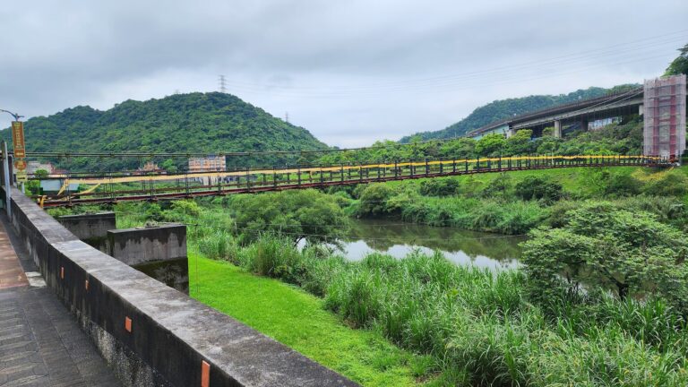 碇內吊橋黃色欄杆橫跨基隆河，兩岸綠意盎然全景，基隆暖暖一日遊地標