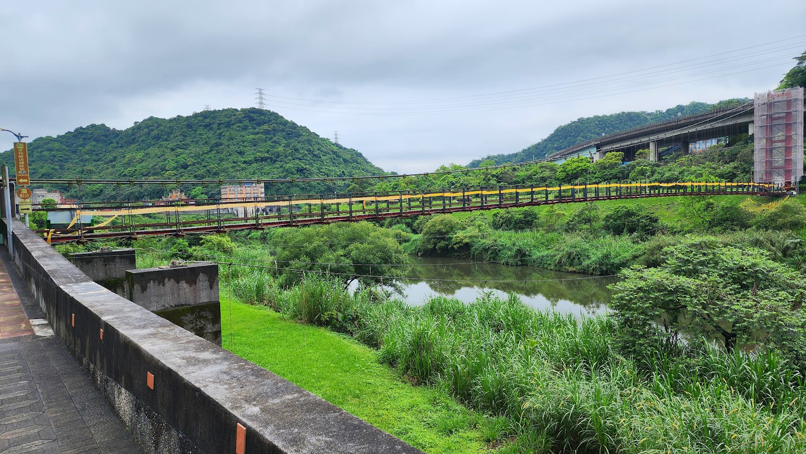碇內吊橋黃色欄杆橫跨基隆河，兩岸綠意盎然全景，基隆暖暖一日遊地標