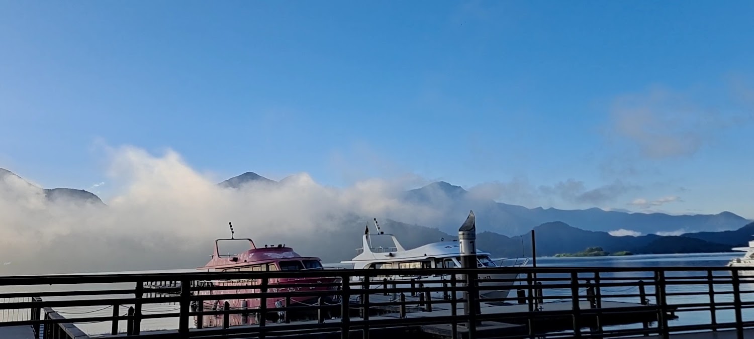 湖邊碼頭停靠兩艘遊艇與遠方雲霧山脈的景色