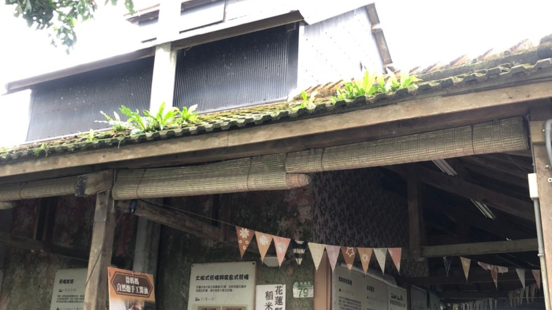 廖快菸樓木造外觀仰角,竹簾遮陽、旗幟飄揚,客家菸樓獨特建築風格