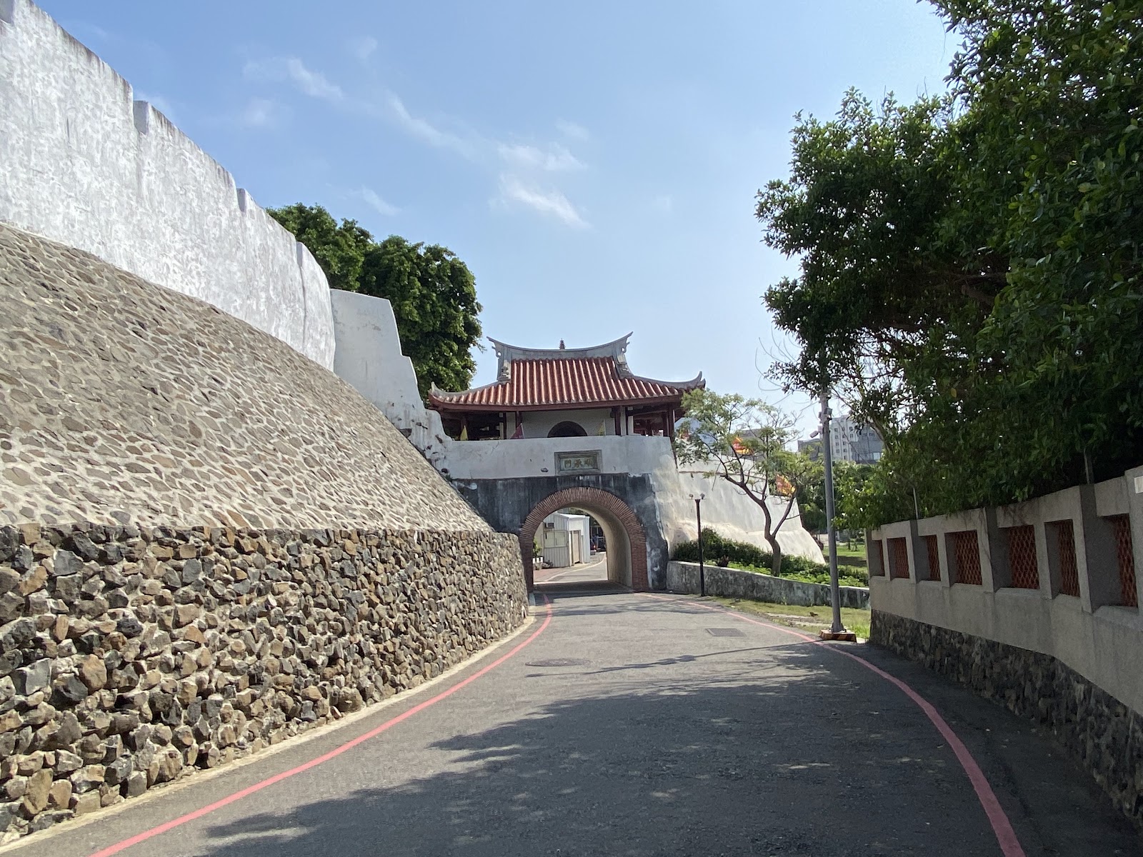 澎湖順承門，石砌城牆護堤道路延伸，傳統閩式城樓拱形磚紅門洞，藍天綠蔭