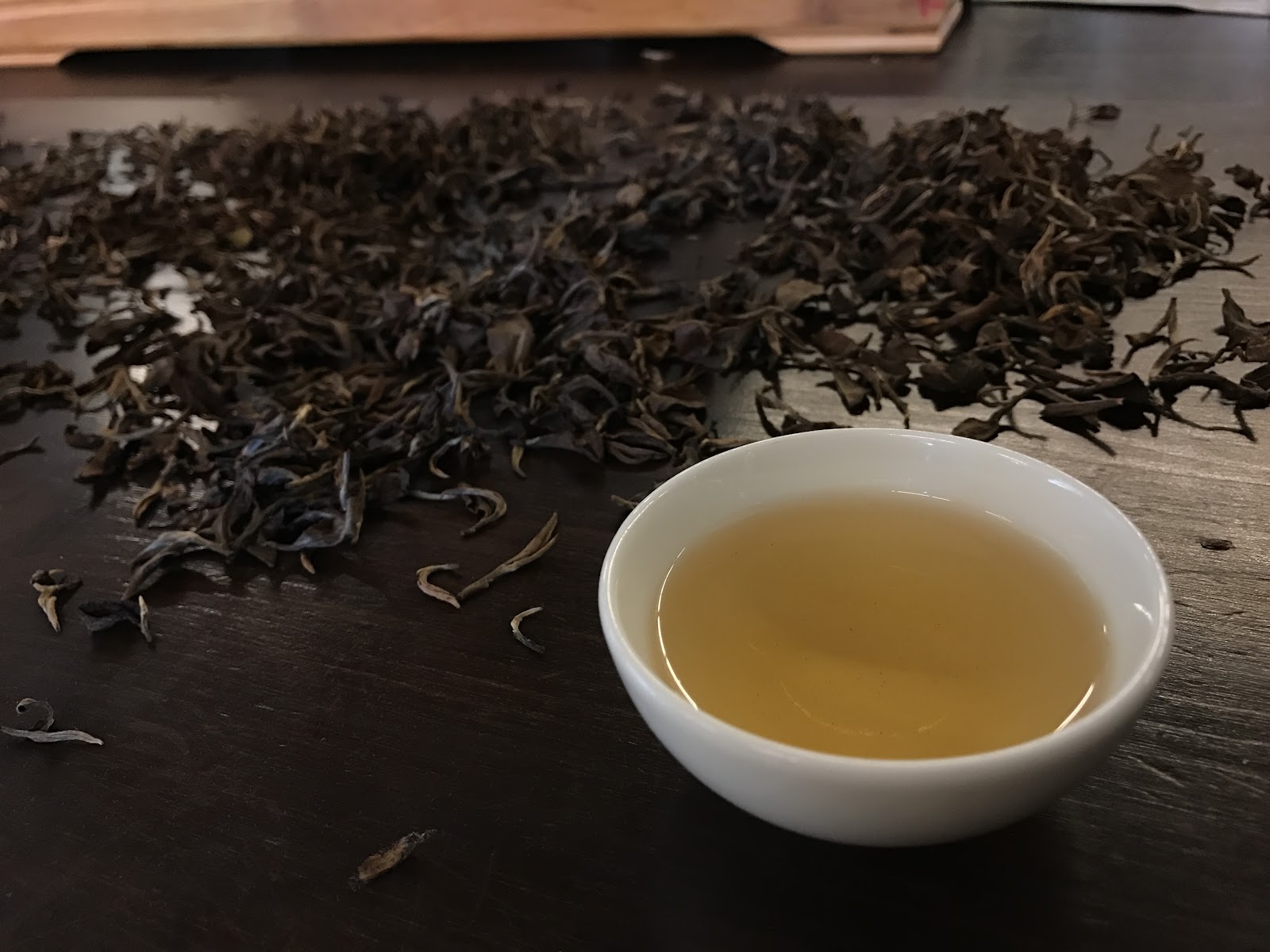 峨眉東方美人茶特寫,茶杯金黃茶湯,茶葉散落桌面