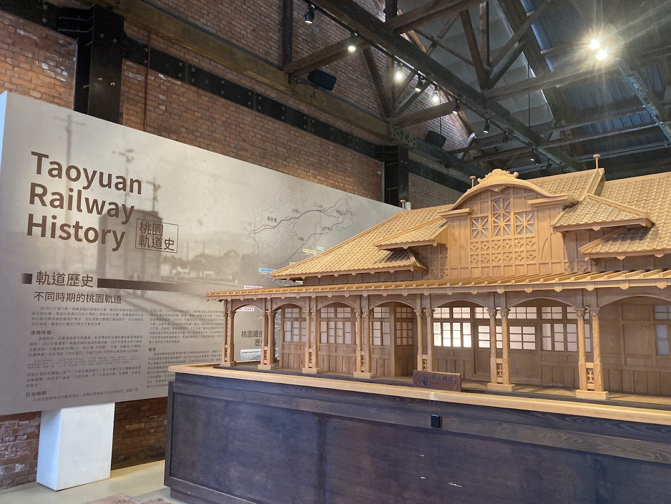 這張圖片展示了桃園鐵道歷史的展覽現場,牆上有介紹文字與地圖,旁邊擺放著一座木造的車站建築模型。圖片無明顯浮水印。
