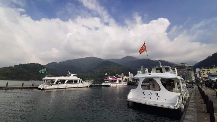 湖邊碼頭多艘遊艇停泊遠處青山與雲朵