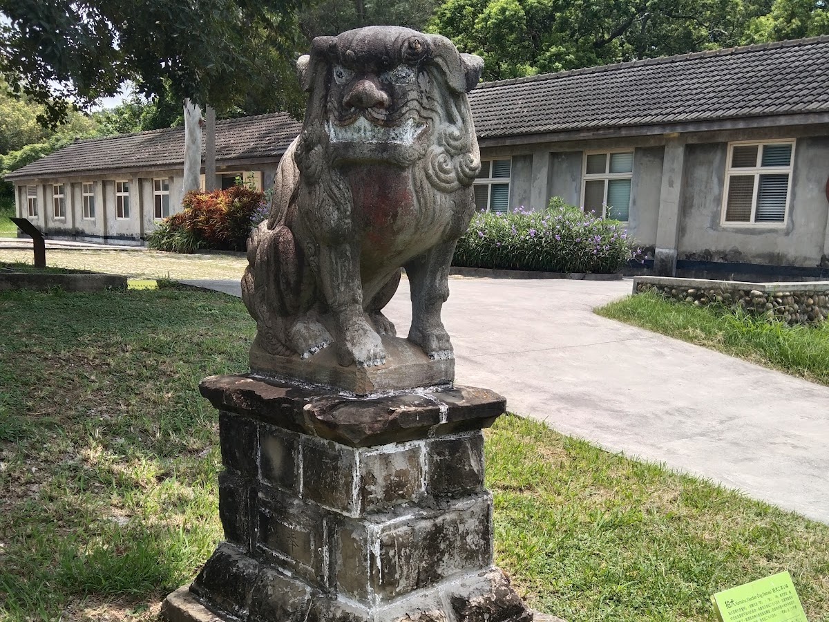 清水神社遺構日式石狛犬立於石台，背景日式低矮平房建築與綠草地