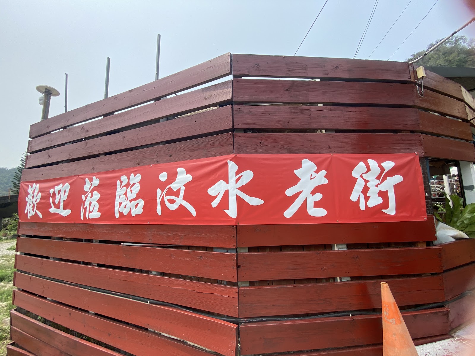 歡迎蒞臨汶水老街紅色橫幅，木板圍牆背景