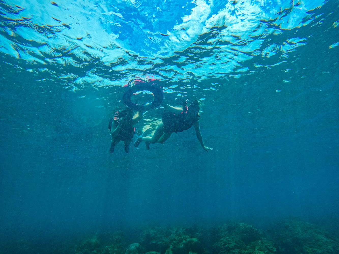 兩人在水下浮潛，穿著救生衣與泳圈探索海中世界