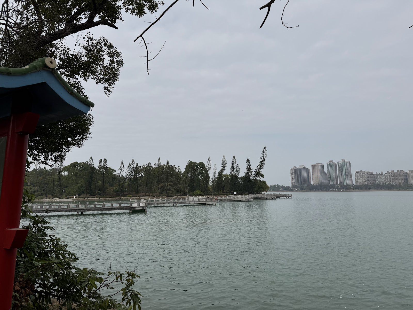澄清湖湖岸亭台欄杆一角,遠景九曲橋與高雄市區大樓,環湖步道散步好去處