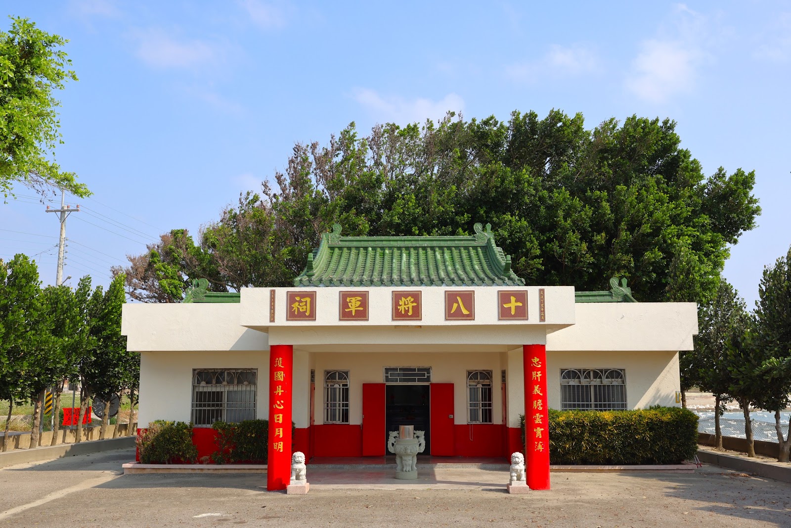 十八將軍祠白牆綠瓦建築外觀，被大榕樹環抱