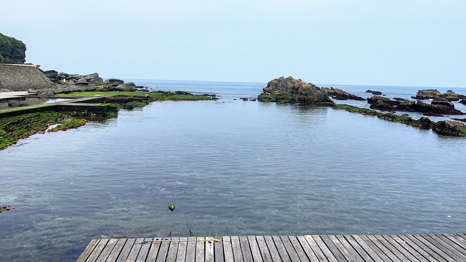 龍洞灣天然潮池全景，前方木棧道，左側岩壁，清澈海水延伸至礁岩外海