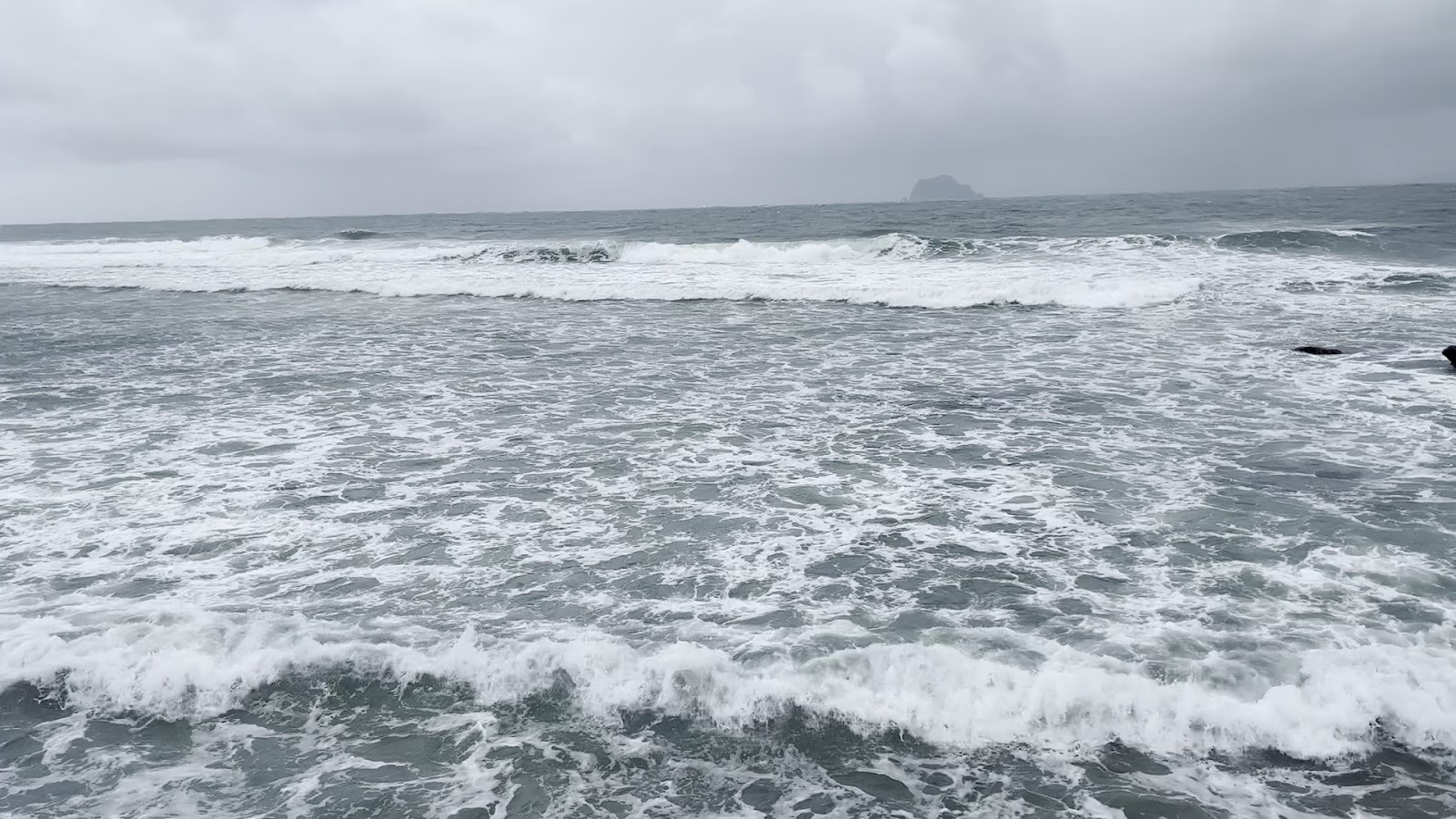 龜吼漁港外海景,陰天海浪滾滾,遠方小島若隱若現