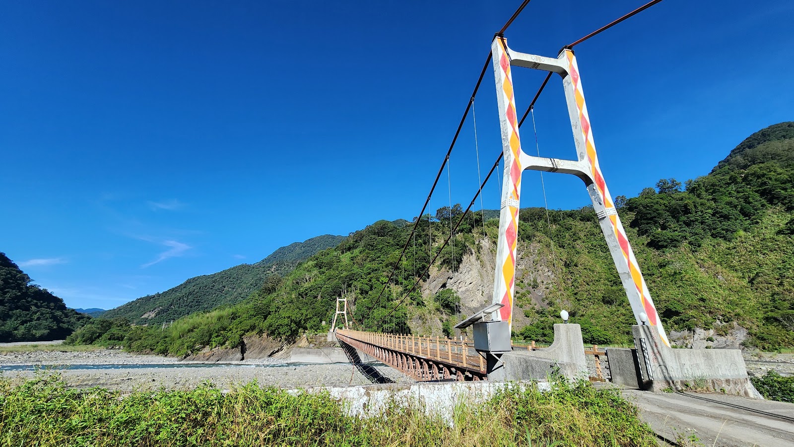 嘎啦鳳吊橋橋塔特寫,橘紅白相間鋼構配上晴朗藍天,橋下可見道路