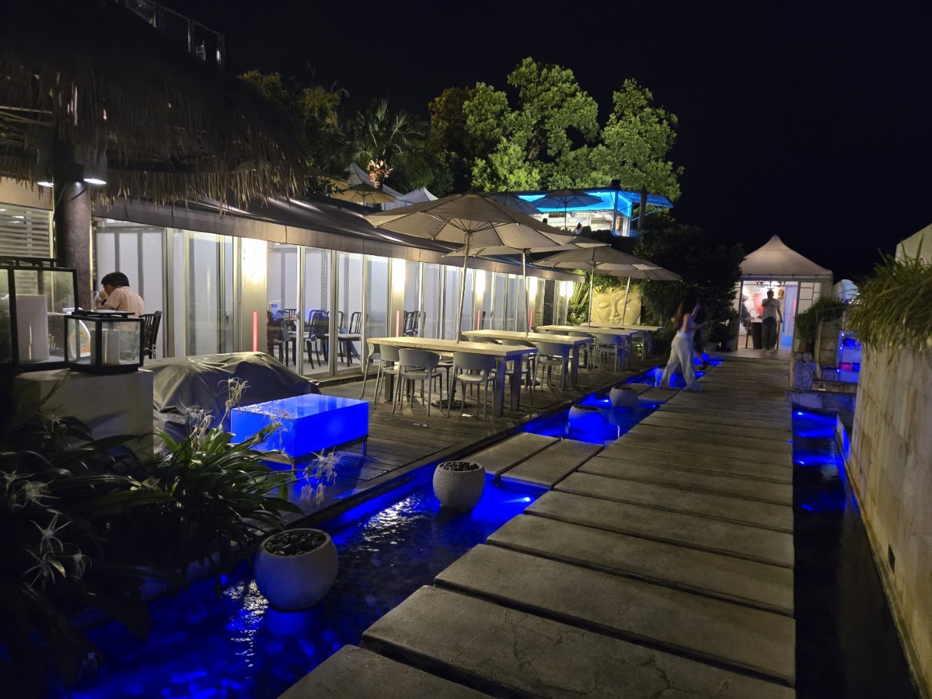 夜晚戶外餐廳有長型步道橫跨水池,水池有藍紫色燈光