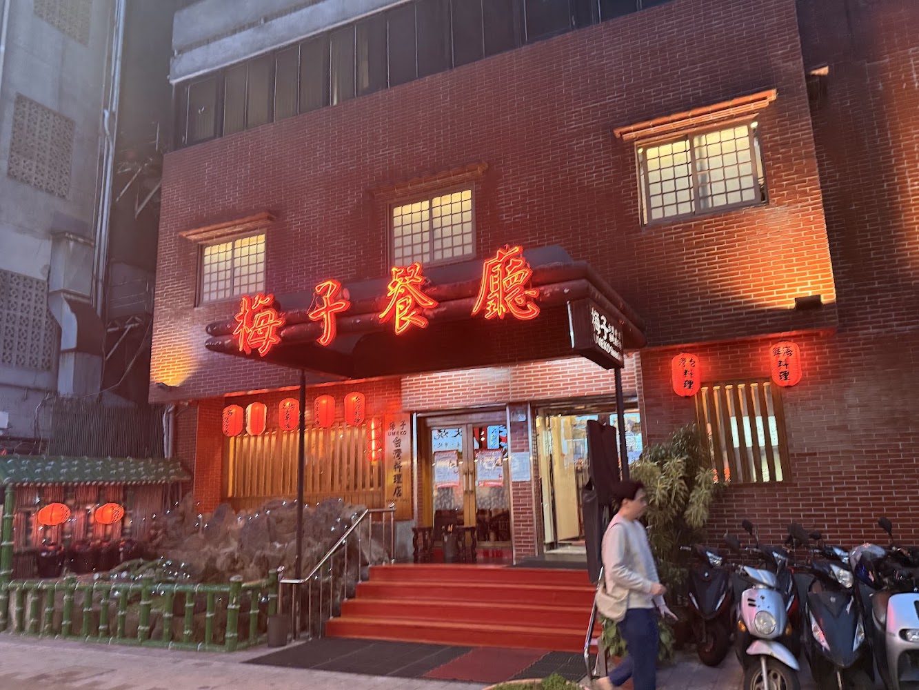 梅子餐廳門口,紅色霓虹燈招牌顯眼,門前有竹子與燈籠