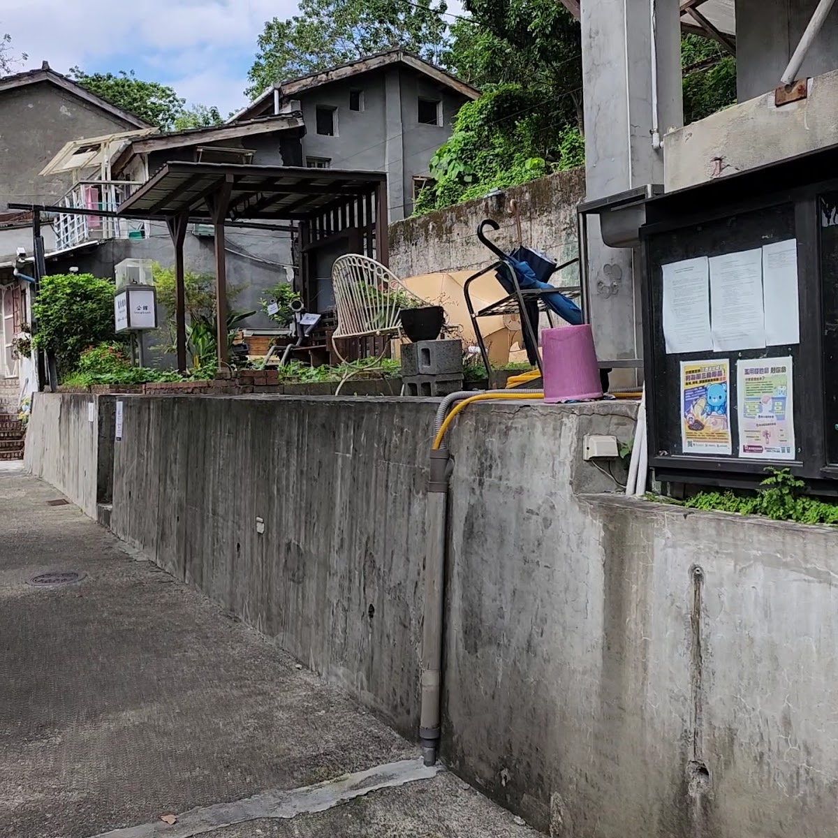 寶藏巖聚落巷弄,混凝土矮牆、藤椅、佈告欄與植物,多層老建築依山而建