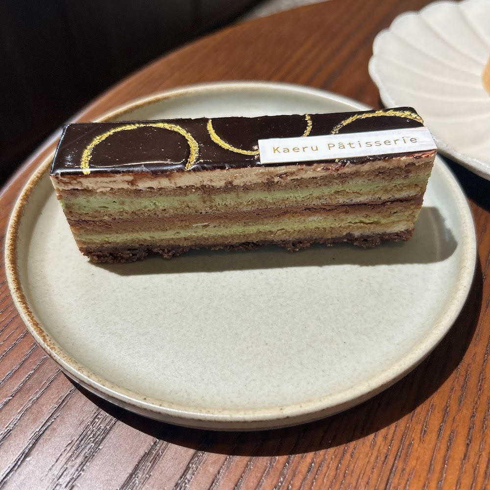 表面有巧克力鏡面與金色裝飾的精緻千層蛋糕，側邊有Kaeru Pâtisserie標籤
