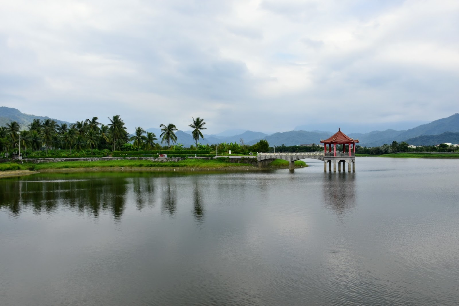 陰天午後的中圳埤湖景,遠方紅亭與拱橋若隱若現,湖面平靜如鏡