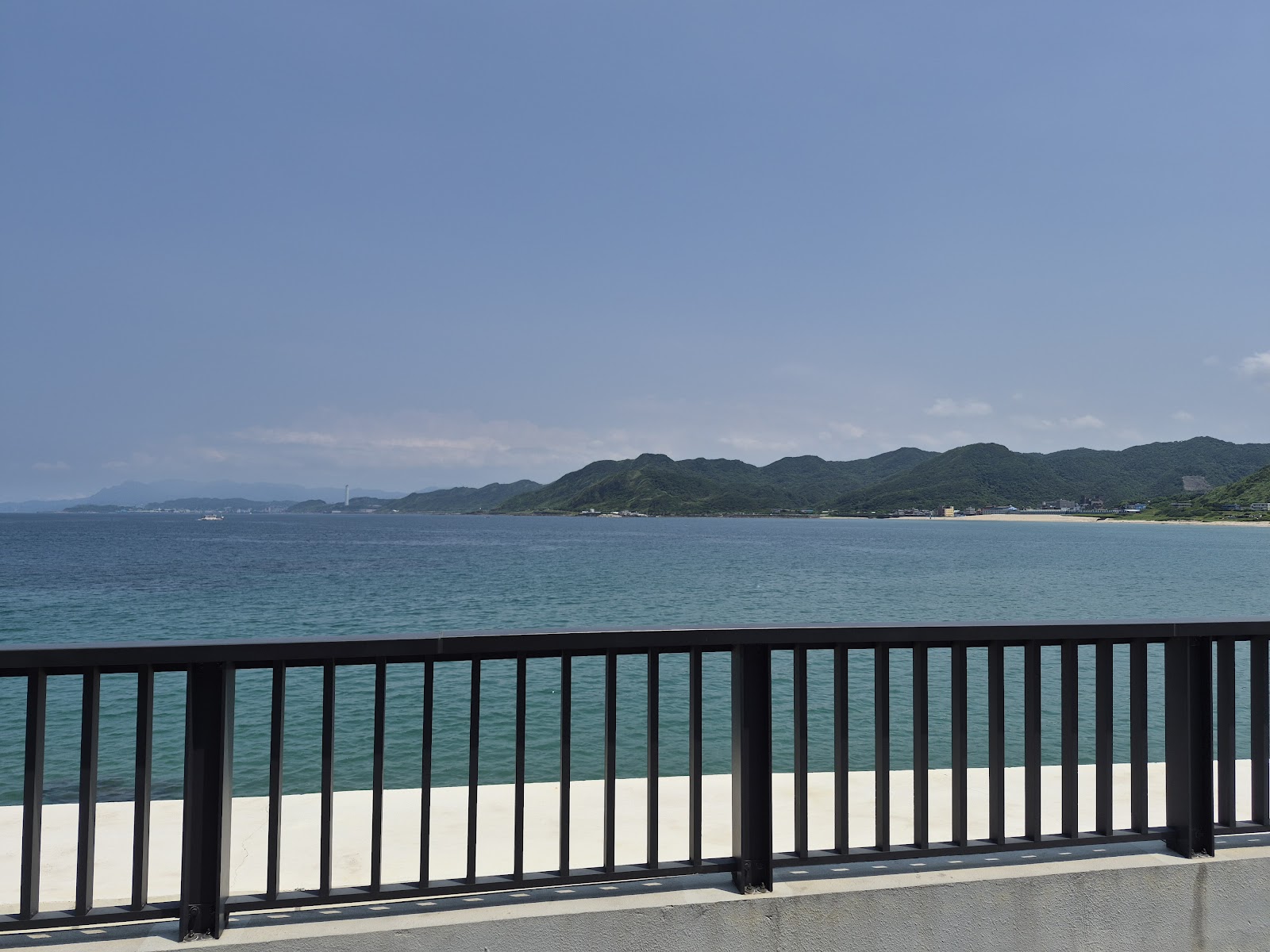龜吼漁夫市集旁海景步道,黑色欄杆,碧藍海水,遠方山丘