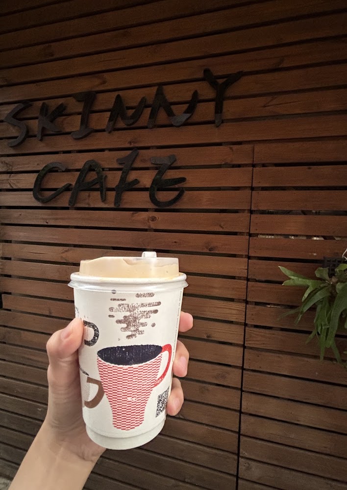 手拿Skinny Cafe外帶咖啡紙杯與店名招牌