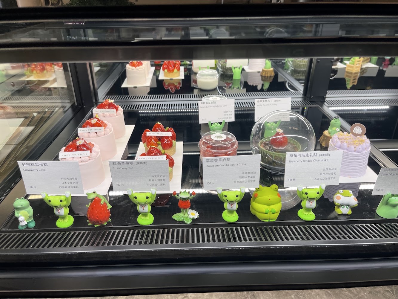 甜點櫃裡擺放草莓蛋糕、草莓塔與奶酪，前方還有青蛙和草莓公仔