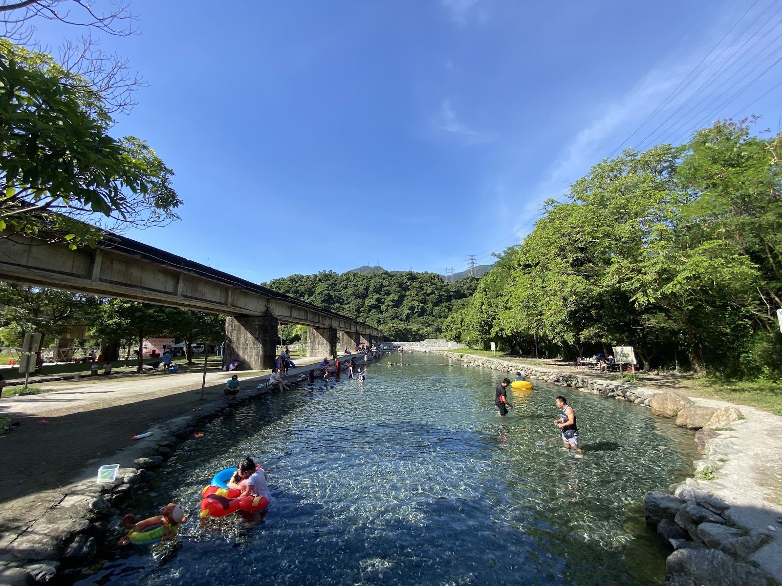 東岳冷泉清澈溪流,北迴鐵路橋墩橫跨上方,遊客悠遊水中