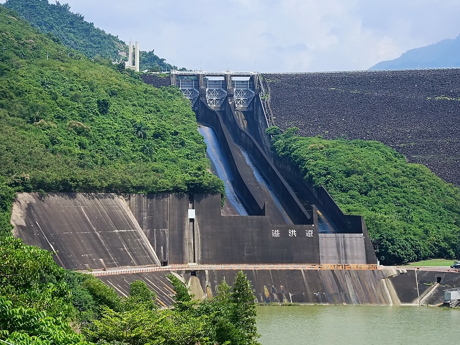 曾文水庫大壩正面景觀，巨型碎石壩面，兩條排水泄洪道，兩側青翠山林