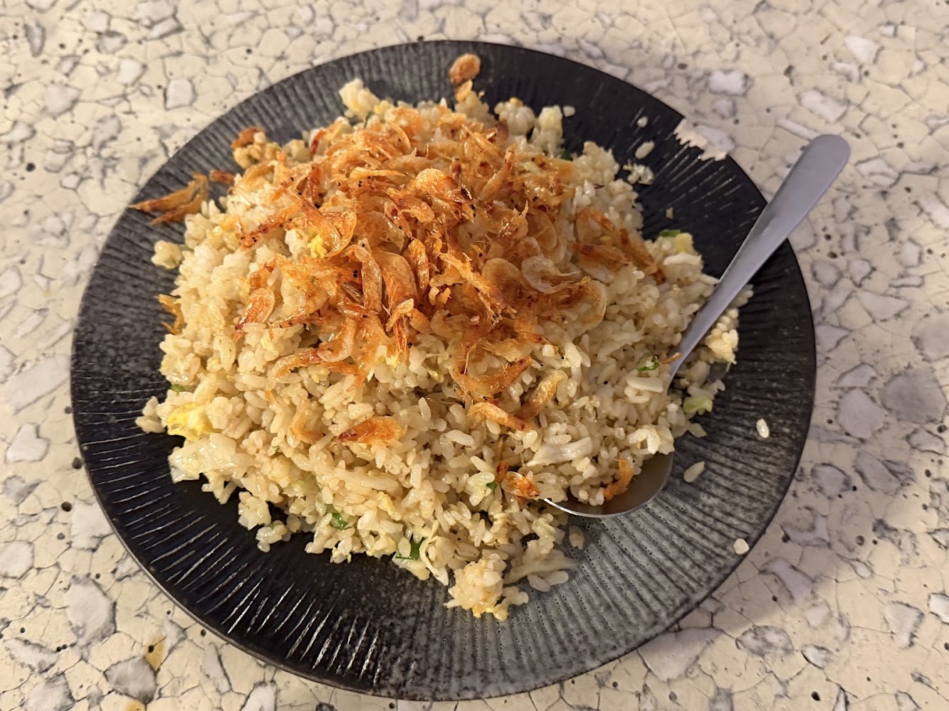 一盤炒飯上面撒有小蝦米,擺放在黑色餐盤中