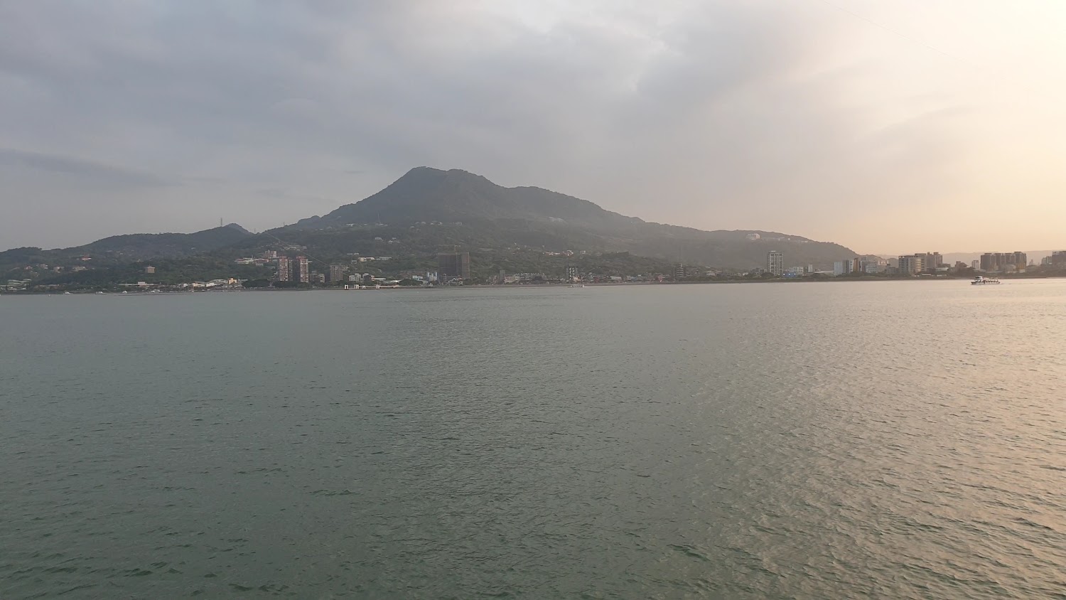 大片河水高山城市建築與右側船隻的傍晚景象