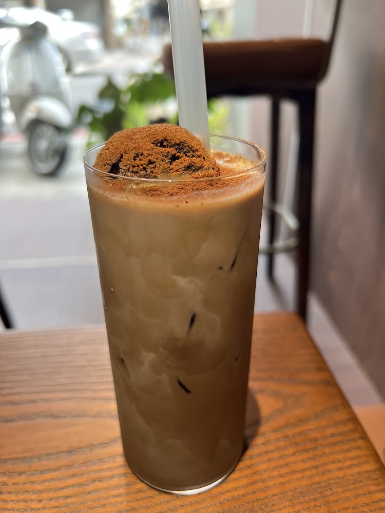 一杯加冰塊的奶茶飲品上灑有可可粉或咖啡粉，放在木桌上