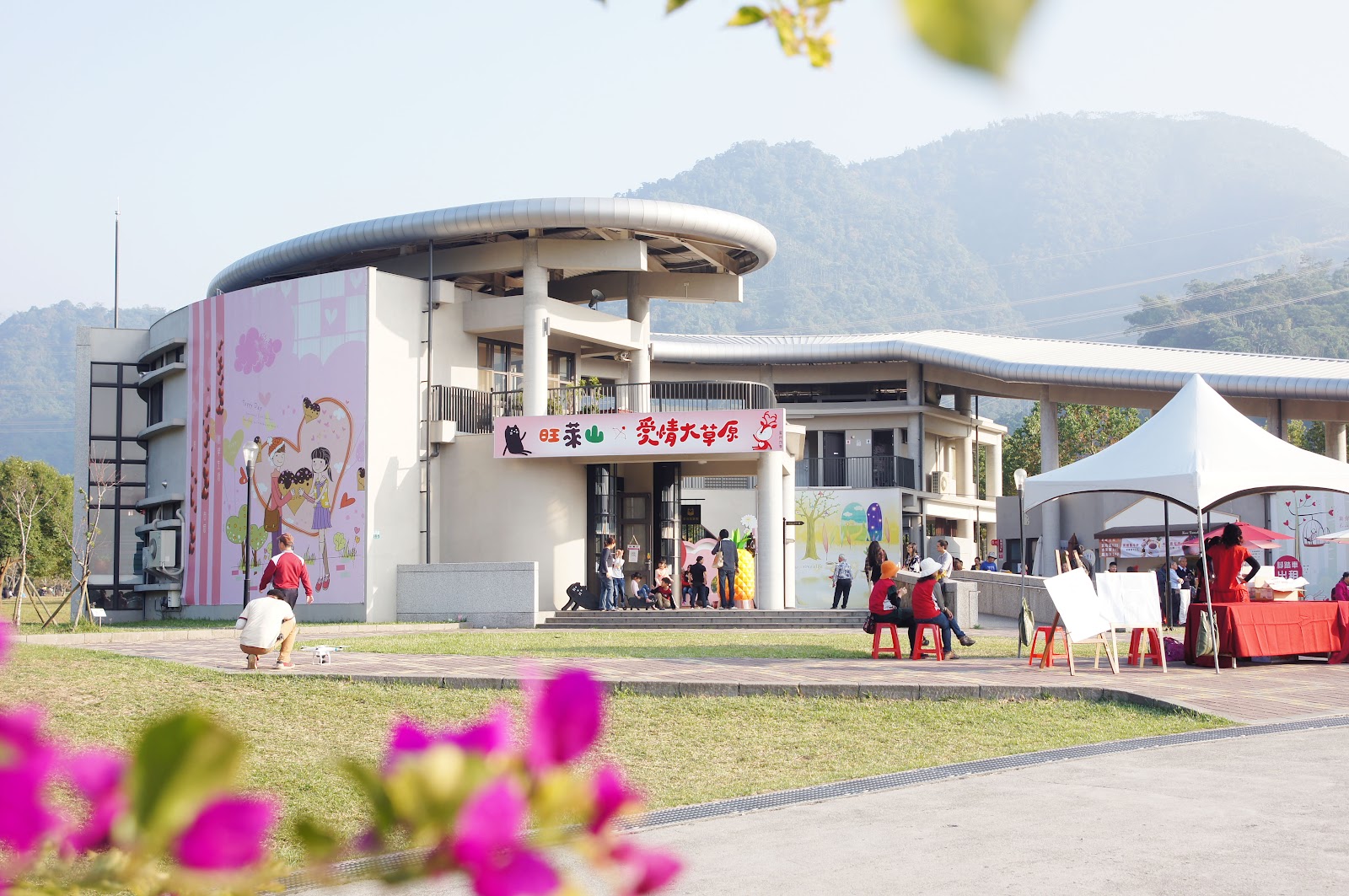 旺萊山門市建築外觀,弧形屋頂設計,前景紫紅色小花,遊客在門口走動