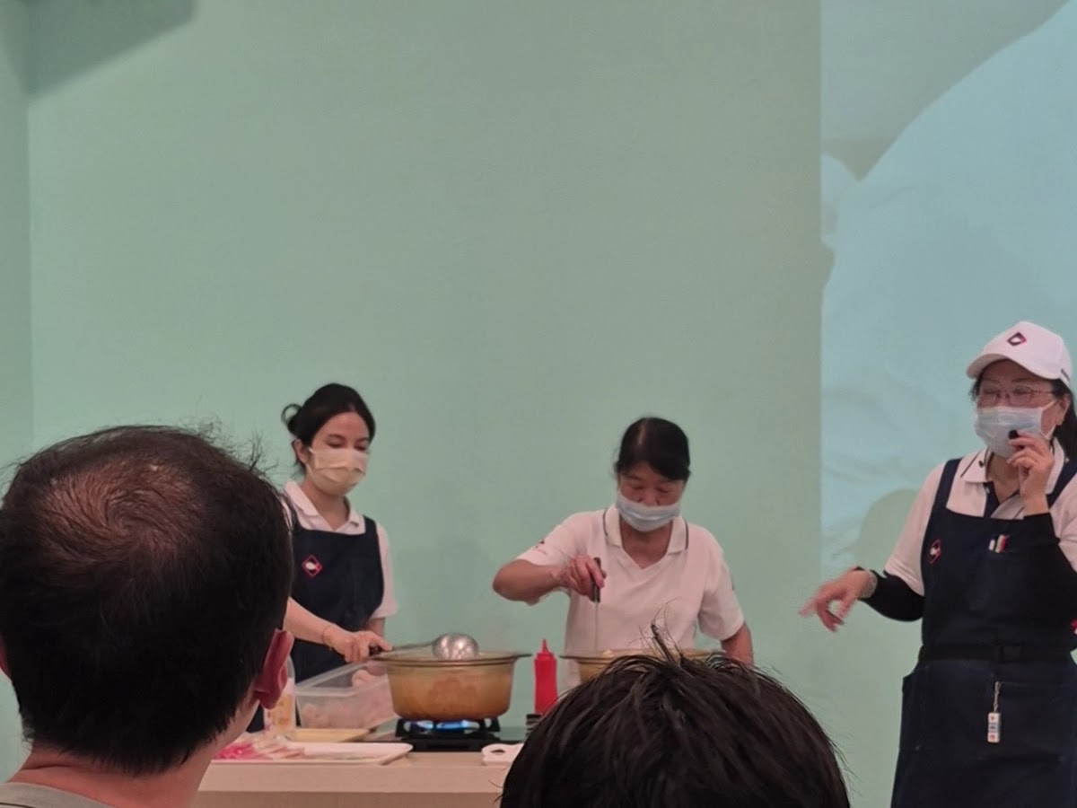 台灣鯛生態創意園區室內食魚教育烹飪示範，示範人員在鍋具前解說，遊客席地聆聽