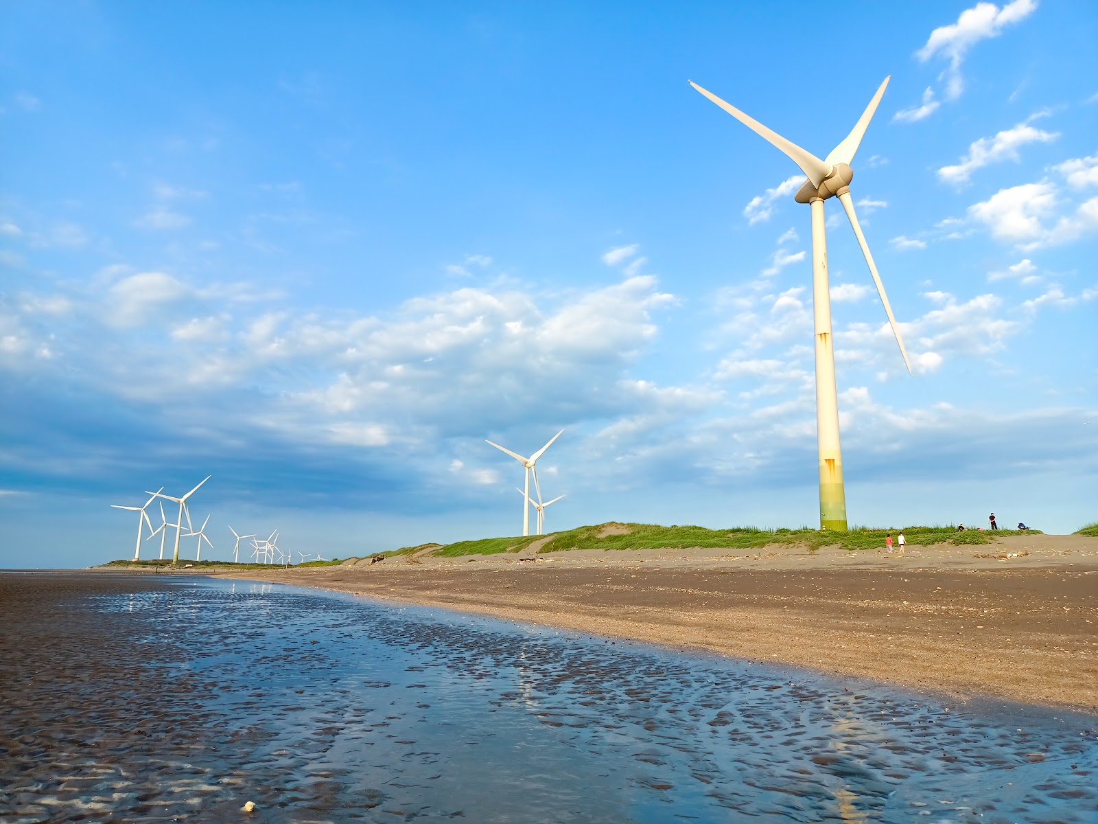 桃園觀音海岸風力發電機群沙灘,藍天白雲遊客散步,壯觀海岸風車景色