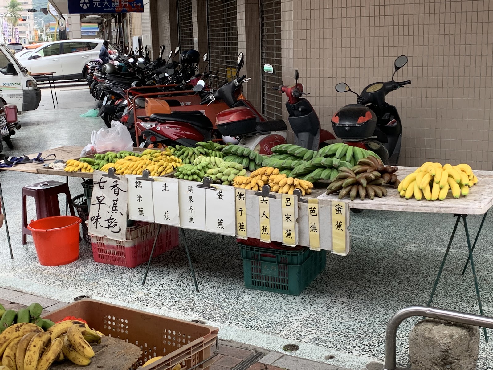 旗山果菜市場外香蕉攤位，多種香蕉品種整齊排列並附品種手寫標示牌