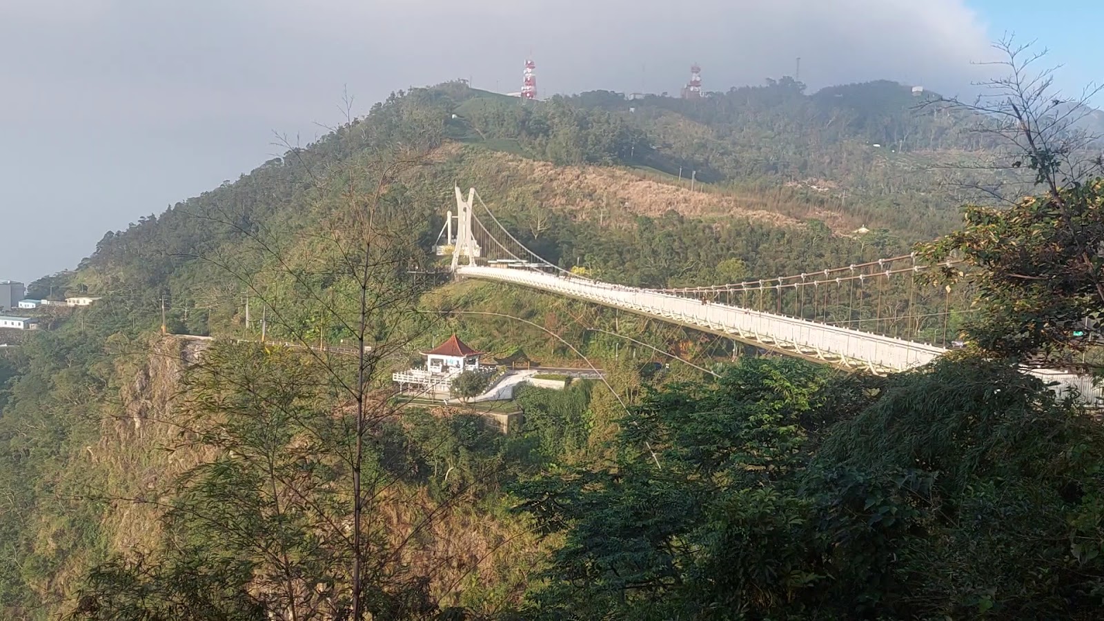 從山腰遠眺太平雲梯吊橋全景,橋橫跨山谷,山頂電波塔,雲霧山景