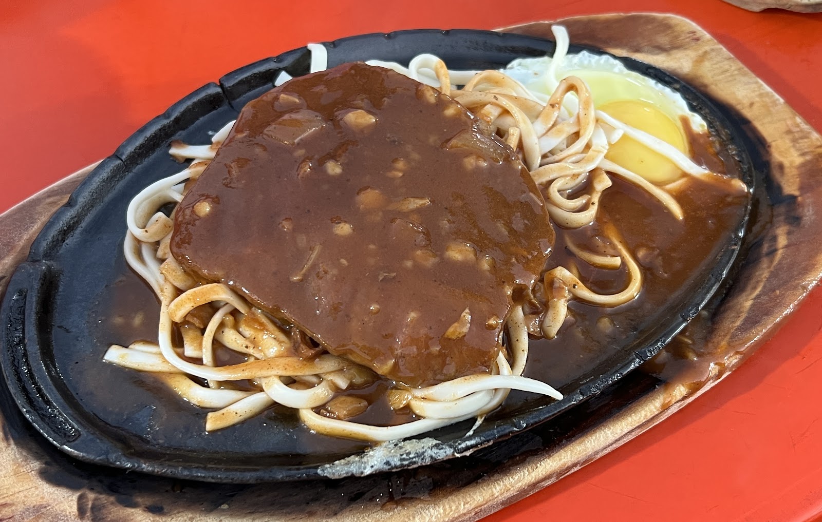 鐵板漢堡排配炒麵,淋上濃郁醬汁,鐵板熱氣騰騰