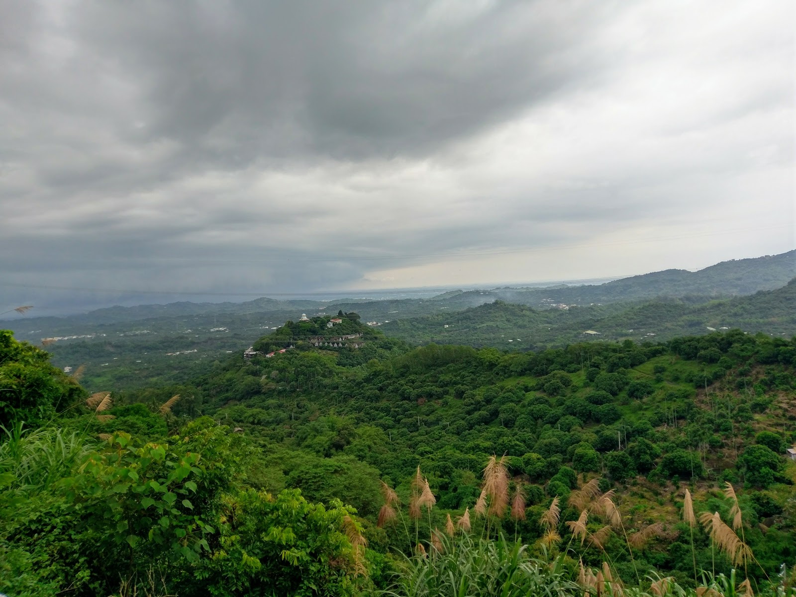 從仙湖休閒農場山頂遠眺連綿翠綠東山丘陵,遠方廟宇隱約可見,雲層壯闊
