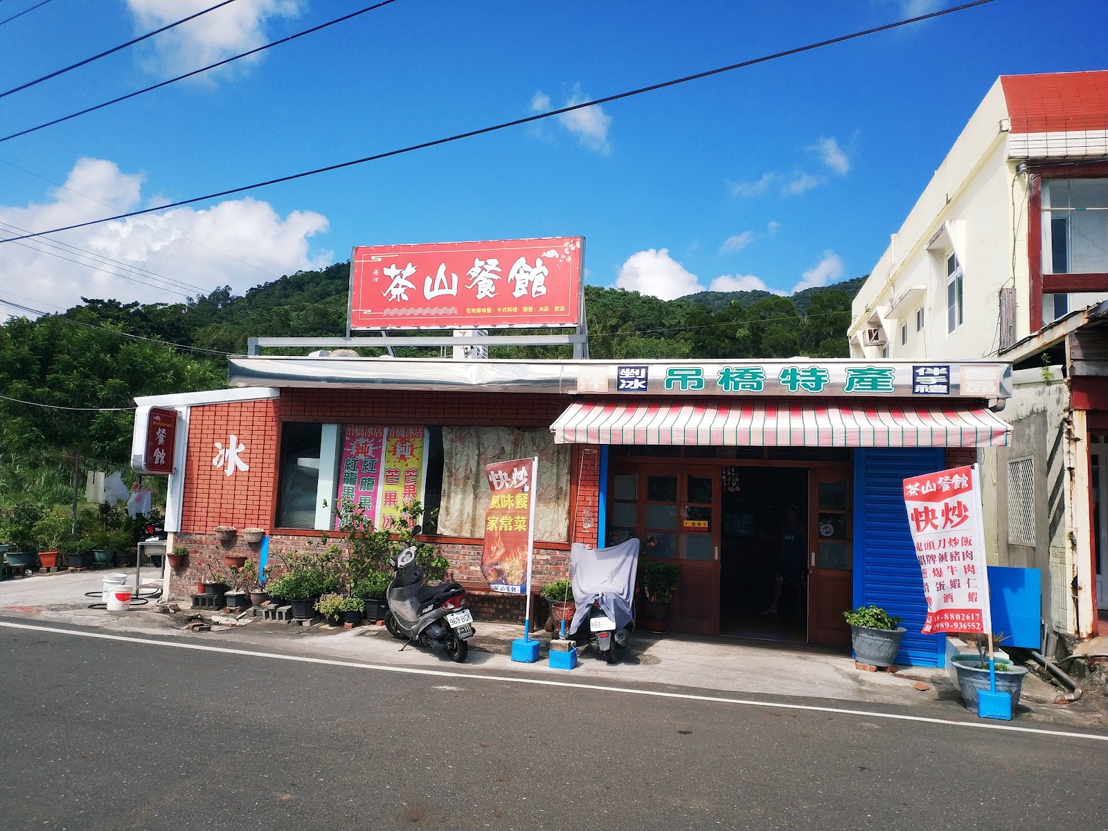 茶山餐館外觀,紅色招牌,旁有吊橋特產商店,停著摩托車,藍天背景
