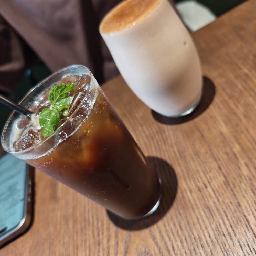 兩杯飲品分別是冰咖啡與奶泡飲，擺放在木桌上