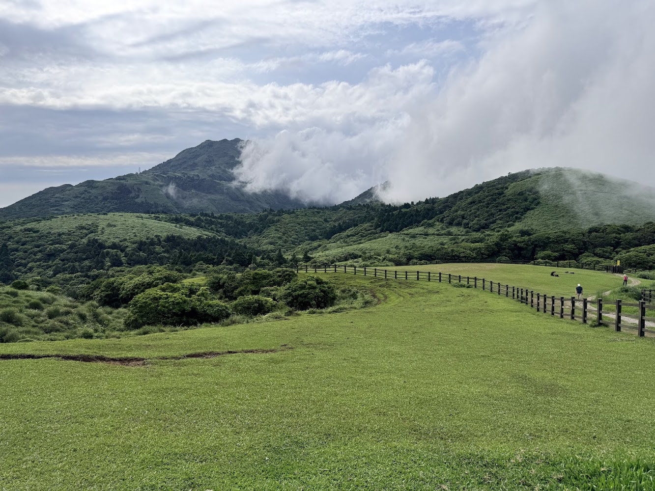 大片翠綠草原與遠方山脈,步道人們散步其中