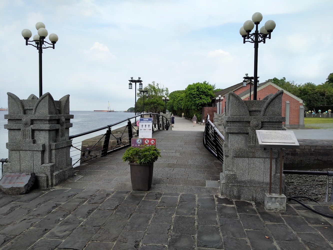 小橋兩側石雕柱與路燈前方花盆告示牌紅磚建築景觀