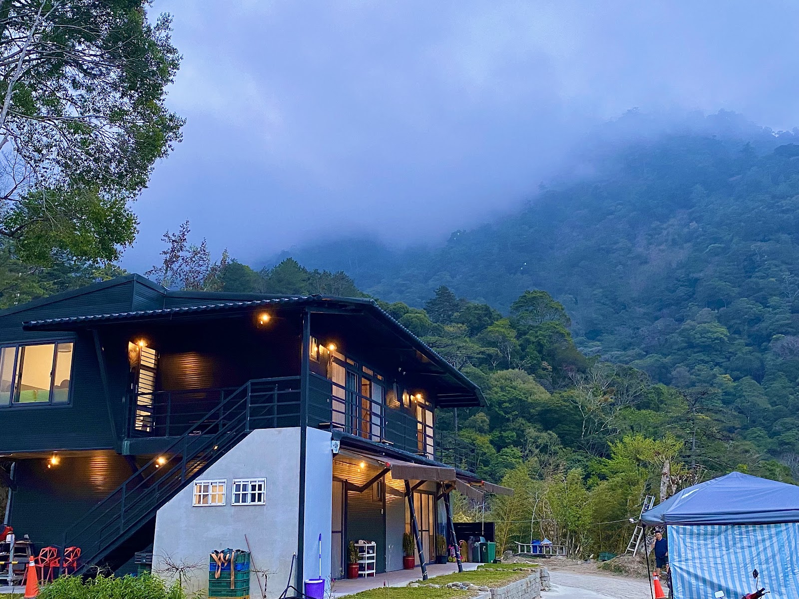 司馬庫斯山間民宿在暮色中亮起燈光,後方是雲霧籠罩的翠綠山嶺,氣氛幽靜安詳