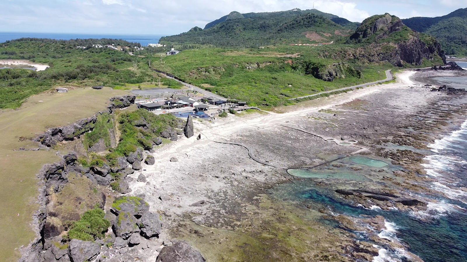 朝日溫泉白天空拍溫泉池珊瑚礁潮間帶高聳山峰背景綠島