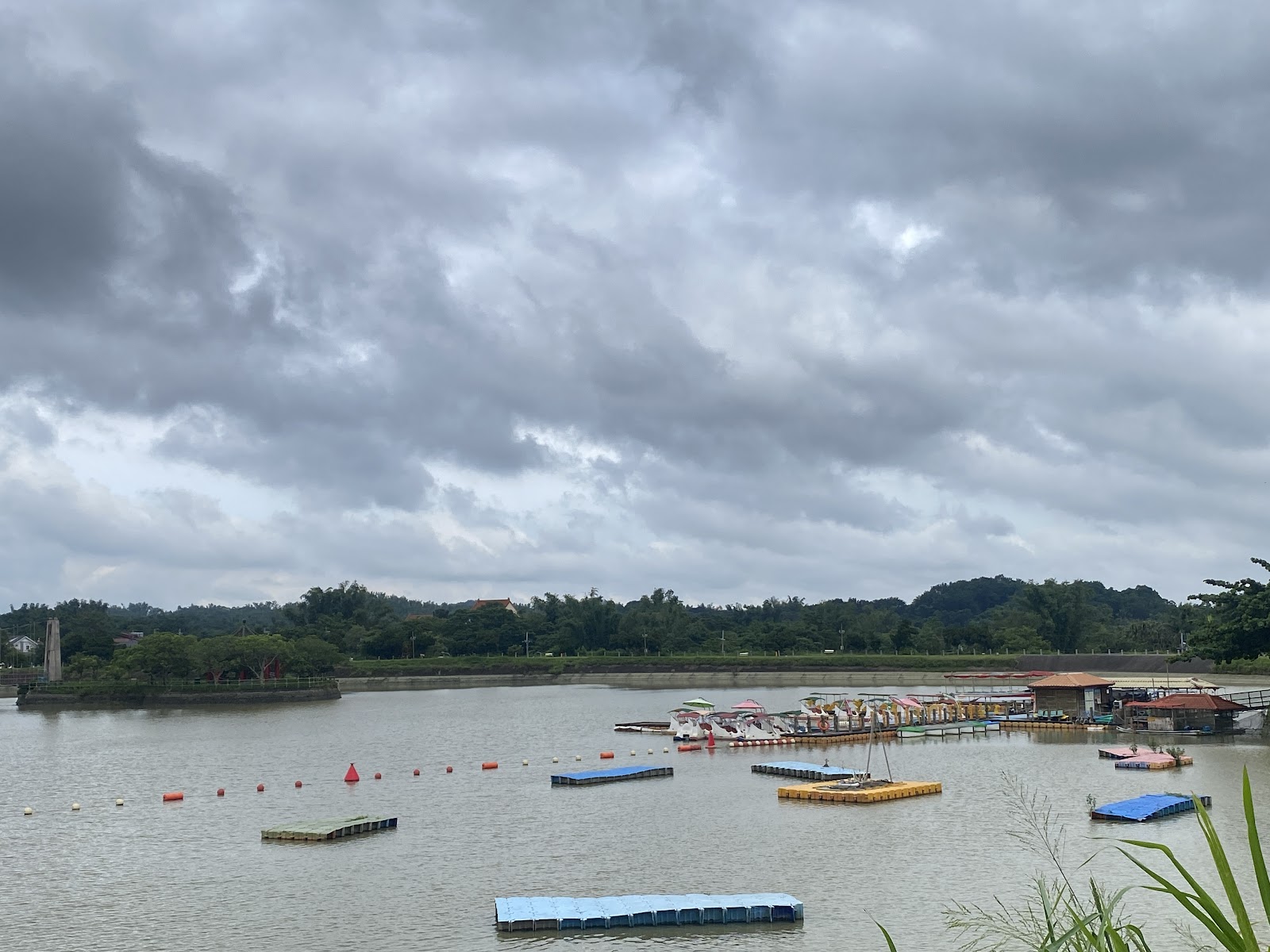 虎頭埤全景,湖面停靠彩色踏板船與浮動碼頭,遠方烤肉木棚