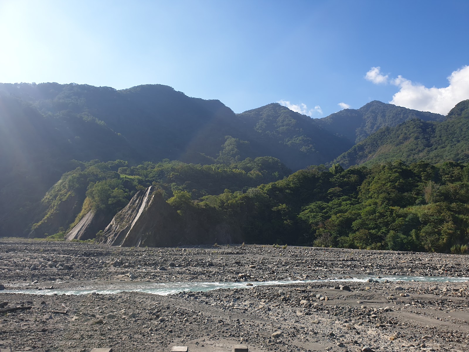 少年溪寬闊礫石河床,遠方山壁可見瀑布水氣,晴天藍天背景