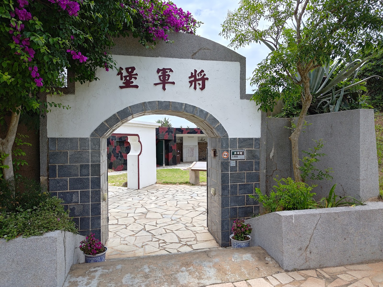 將軍堡白色拱形入口，兩側紫色九重葛盛開，可見內部庭院