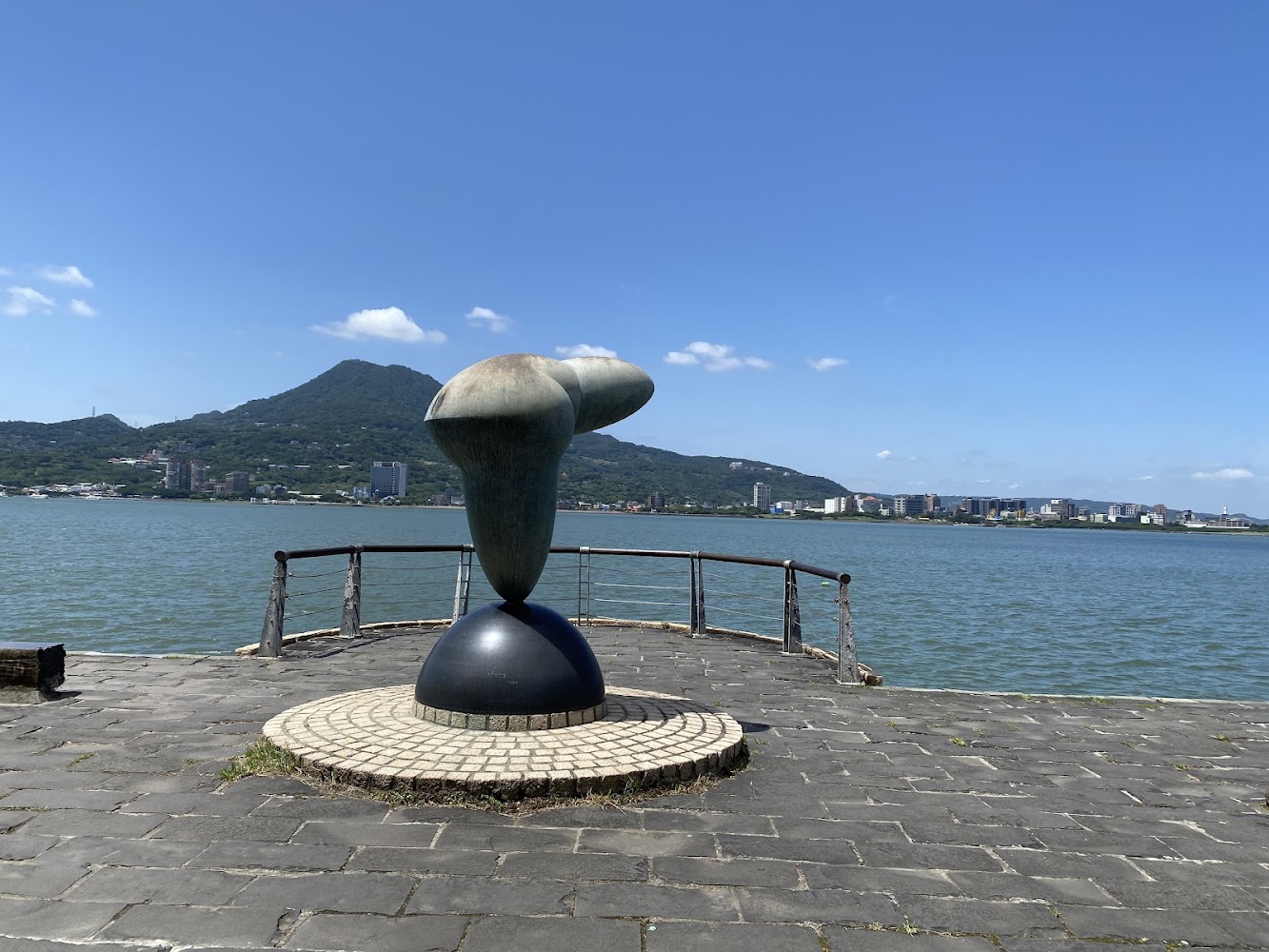 河岸平台上的現代藝術雕塑與遠方山景城市景觀