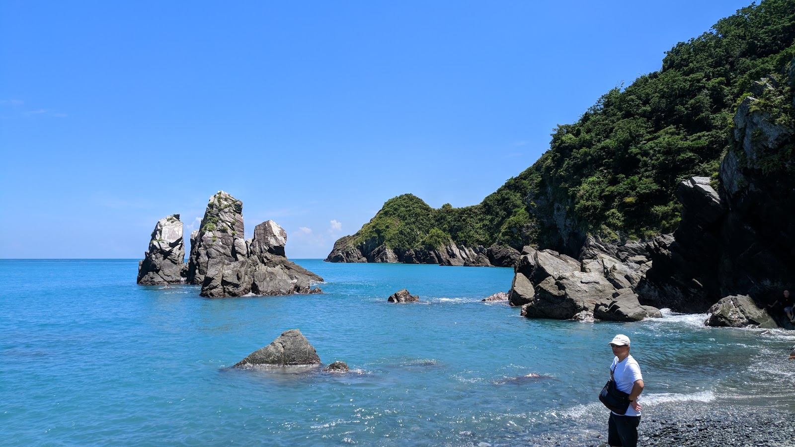 玄武岩柱群全景,遊客站立岩石之間,天空晴朗,大海碧藍