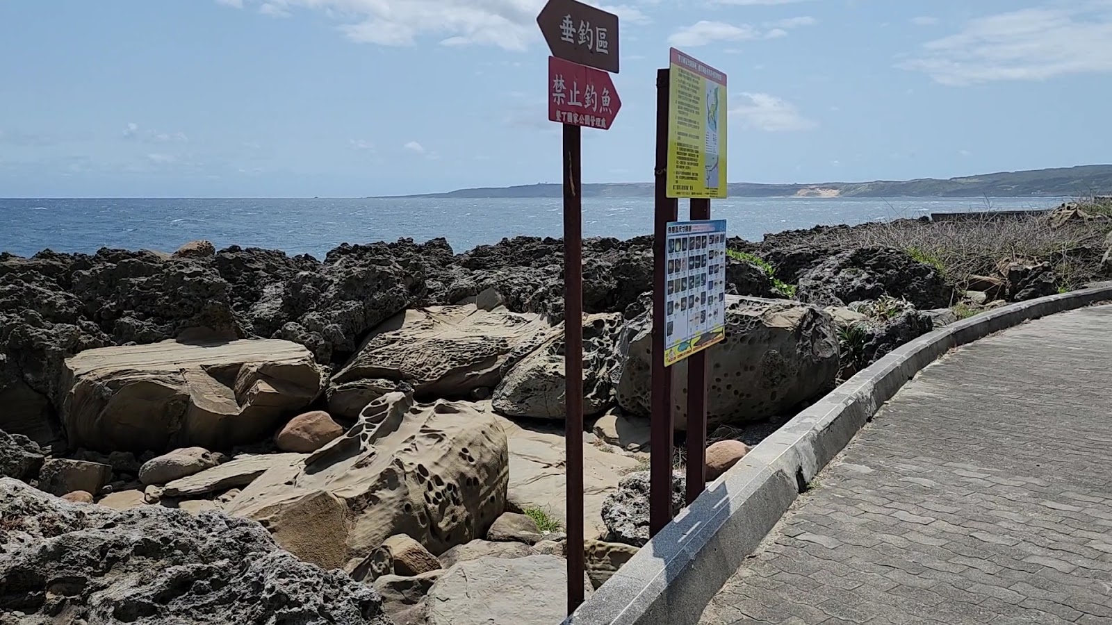 佳樂水海岸步道與指示牌,背景是黑色海蝕礁岩與蔚藍海洋