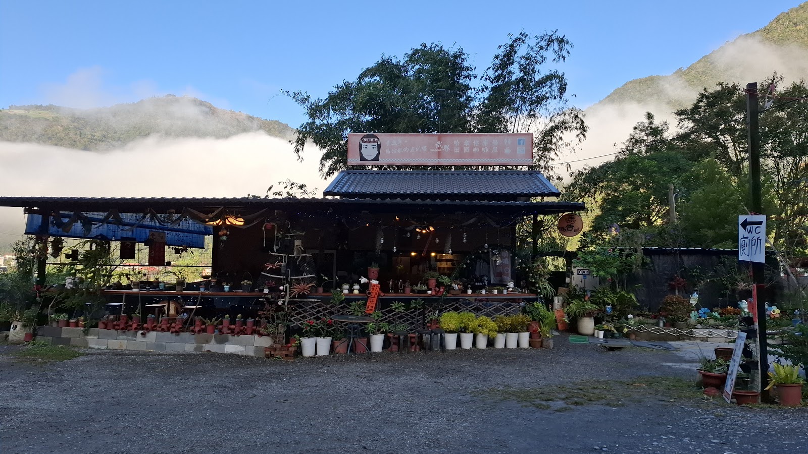 武界哈拿花園咖啡屋外觀,木造小屋前擺滿盆栽,背後是雲霧繚繞的山林