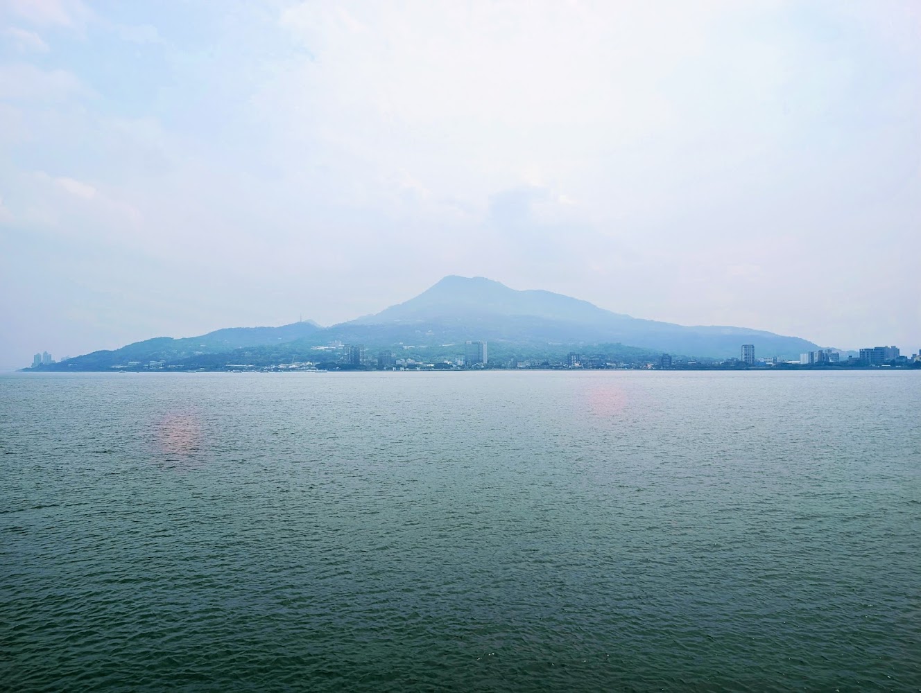 寬廣水域遠方山脈與城市建築淡藍天空景緻